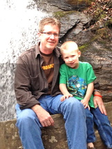 A man and a boy sitting next to a waterfall.
