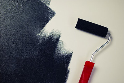 A paint roller with black paint on a white wall.