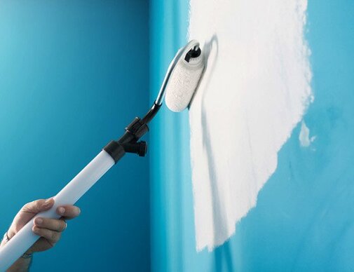 A person using a paint brush to paint a blue wall.